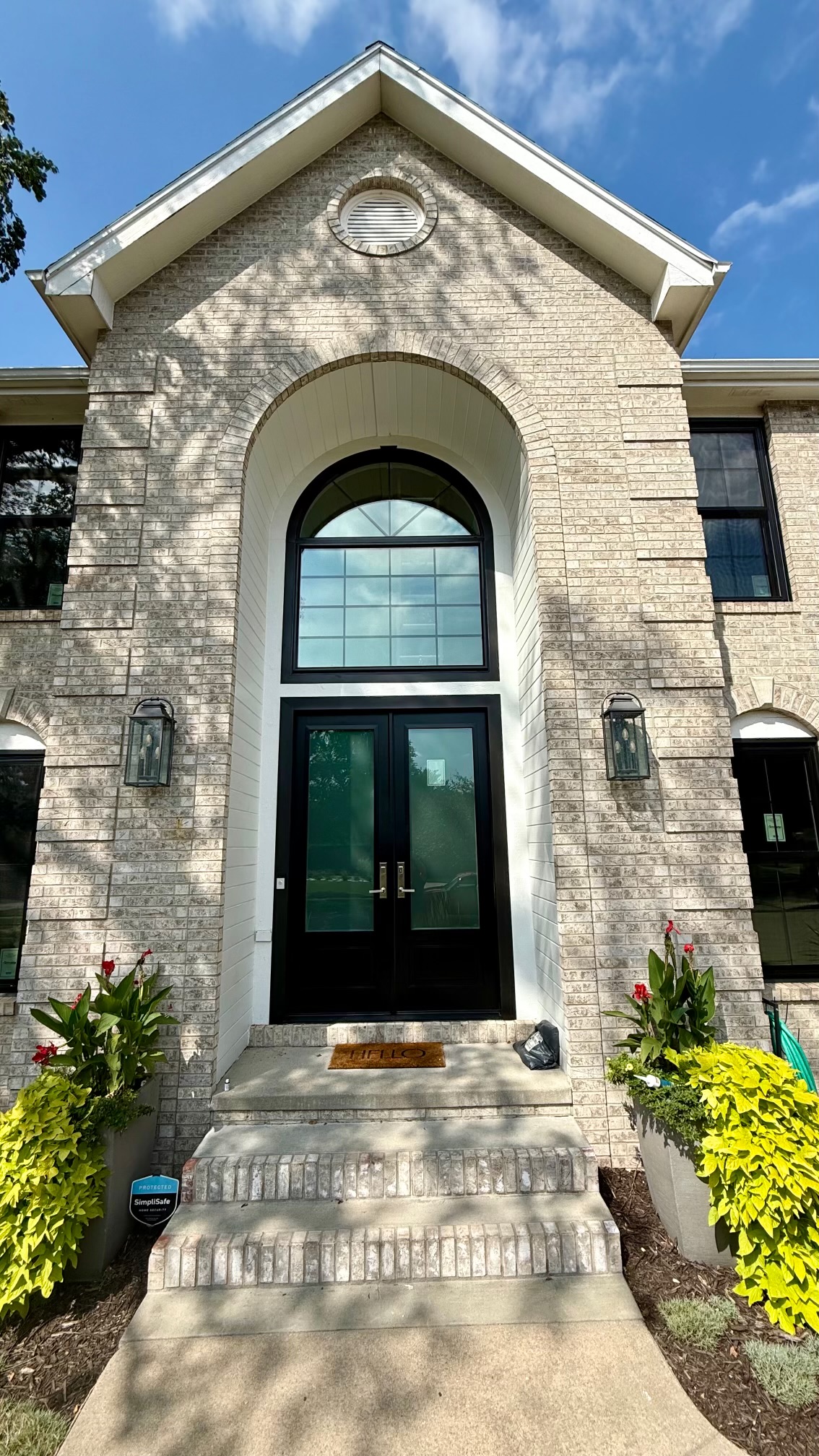 Black double entry doors with arched transom and matching windows on a brick home